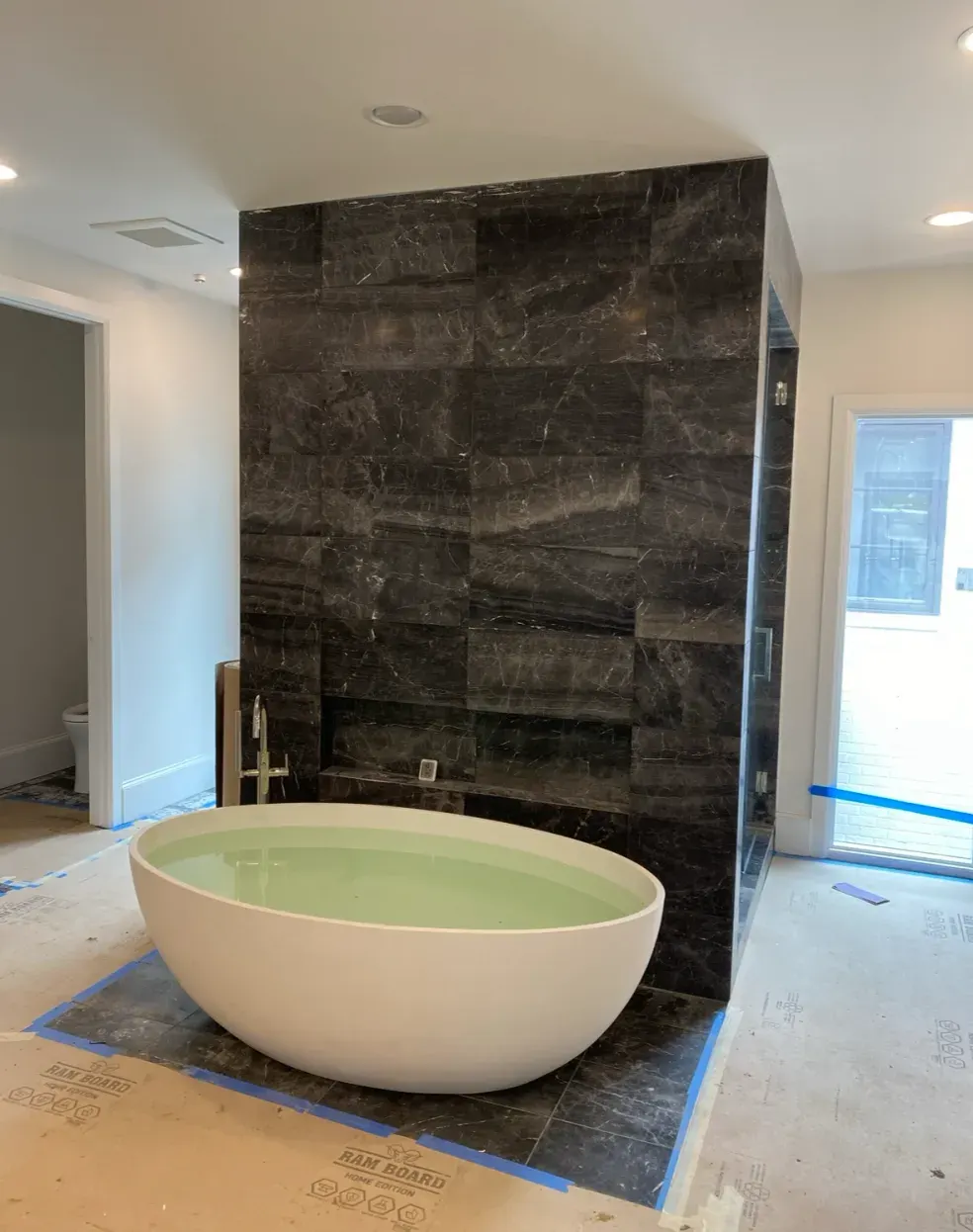 Dramatic dark-marble feature wall behind a sculptural soaking tub
