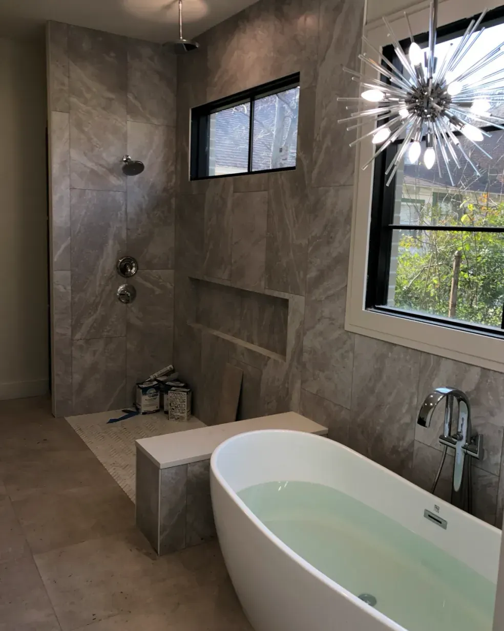 Gray tile bath with a freestanding tub and sputnik chandelier