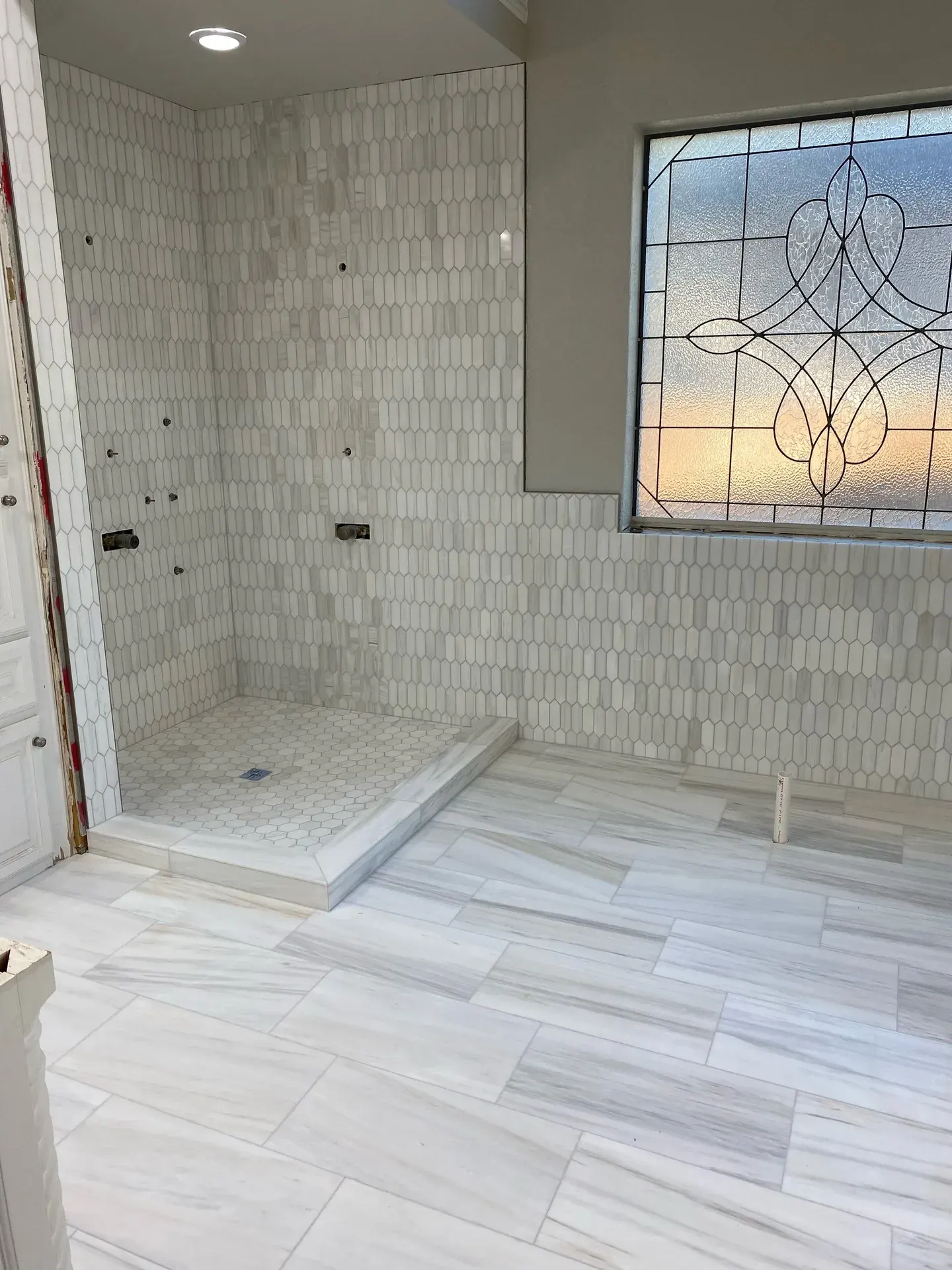 White marble bathroom with a walk-in shower and a leaded stained-glass window
