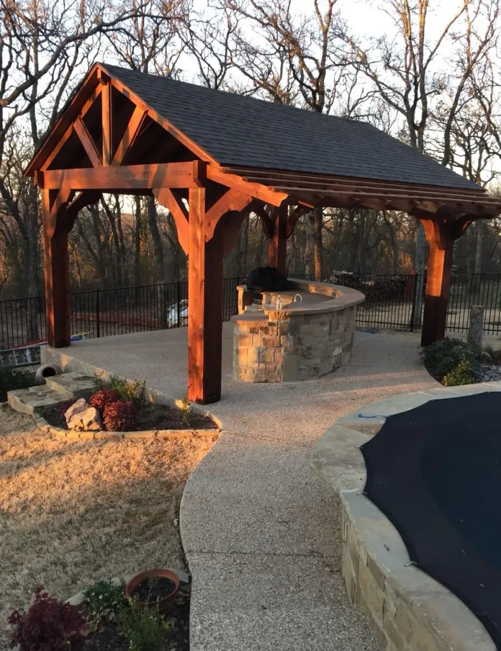 Stained timber pavilion with a stone outdoor bar beside the pool at sunset