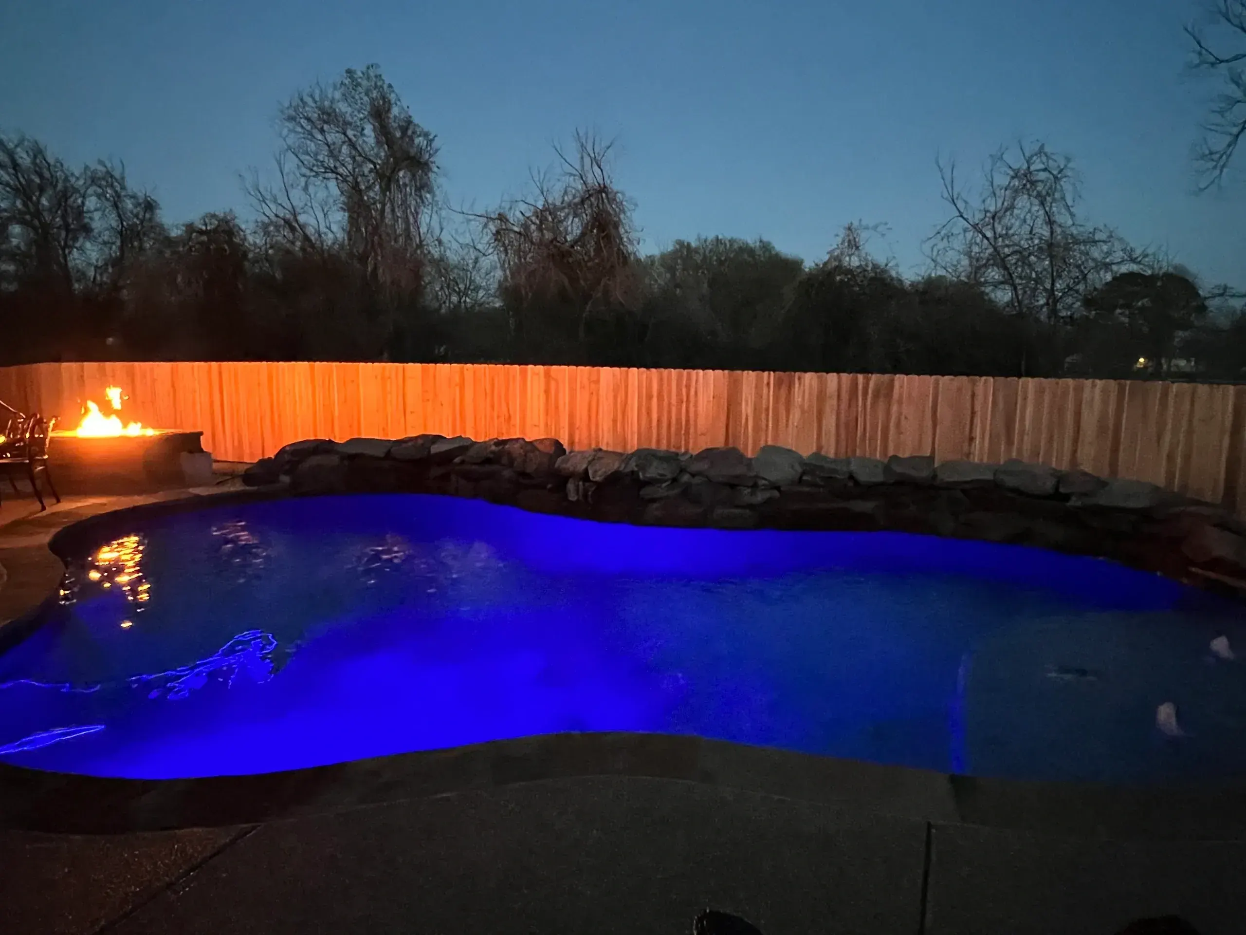 Freeform pool lit blue at dusk with a fire feature and a new cedar privacy fence