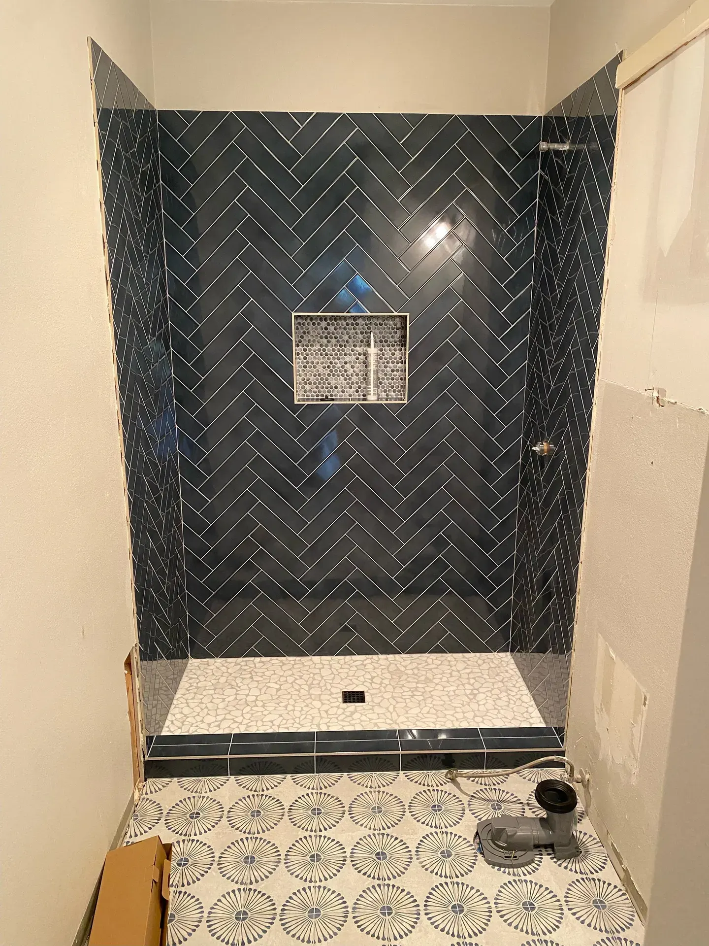 Navy herringbone tile shower with a pebble floor and mosaic niche